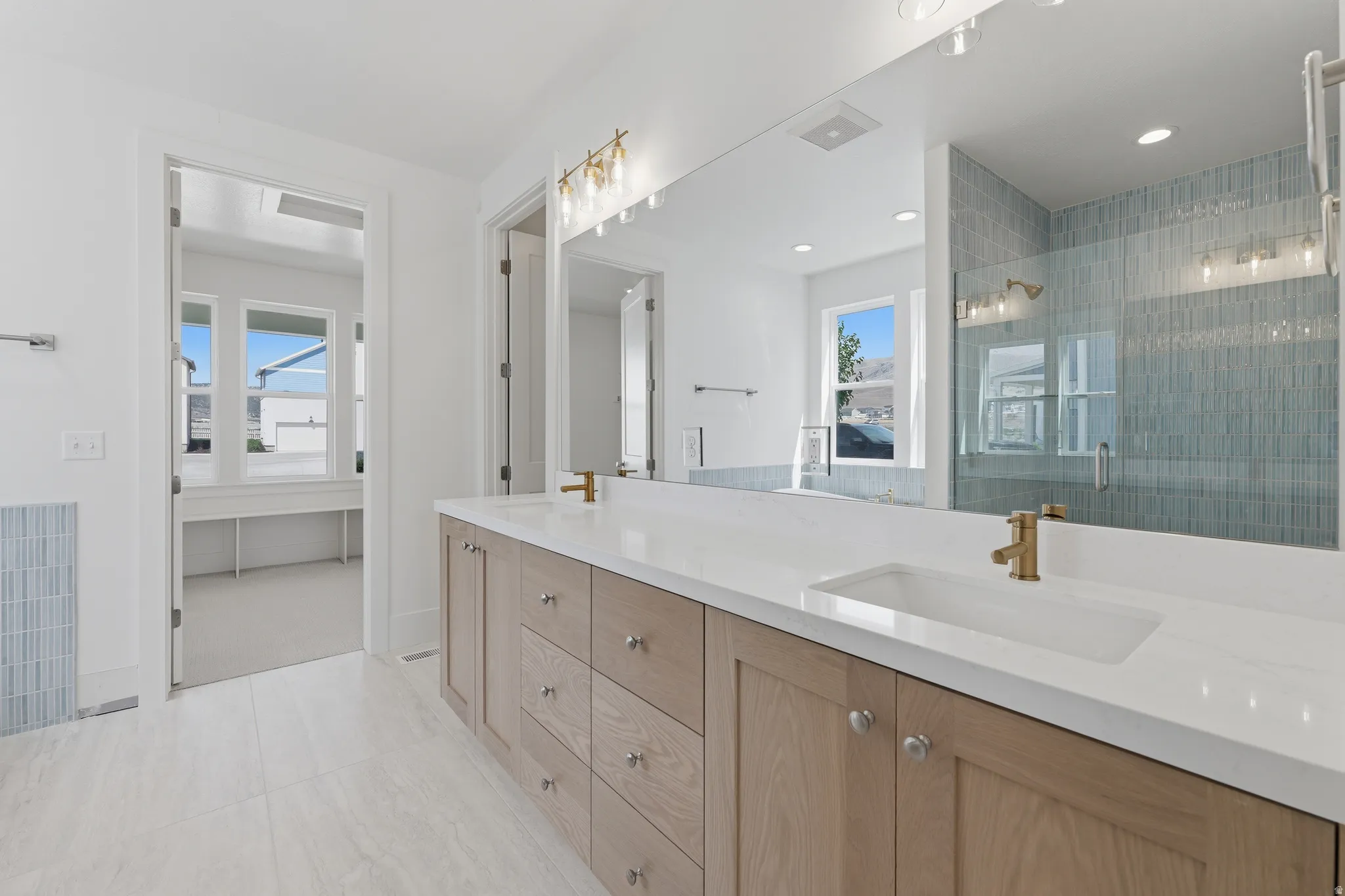 Primary Suite. Dual vanity with light wood-finish cabinetry, white countertops, rectangular undermount sinks, and brass-finish fixtures