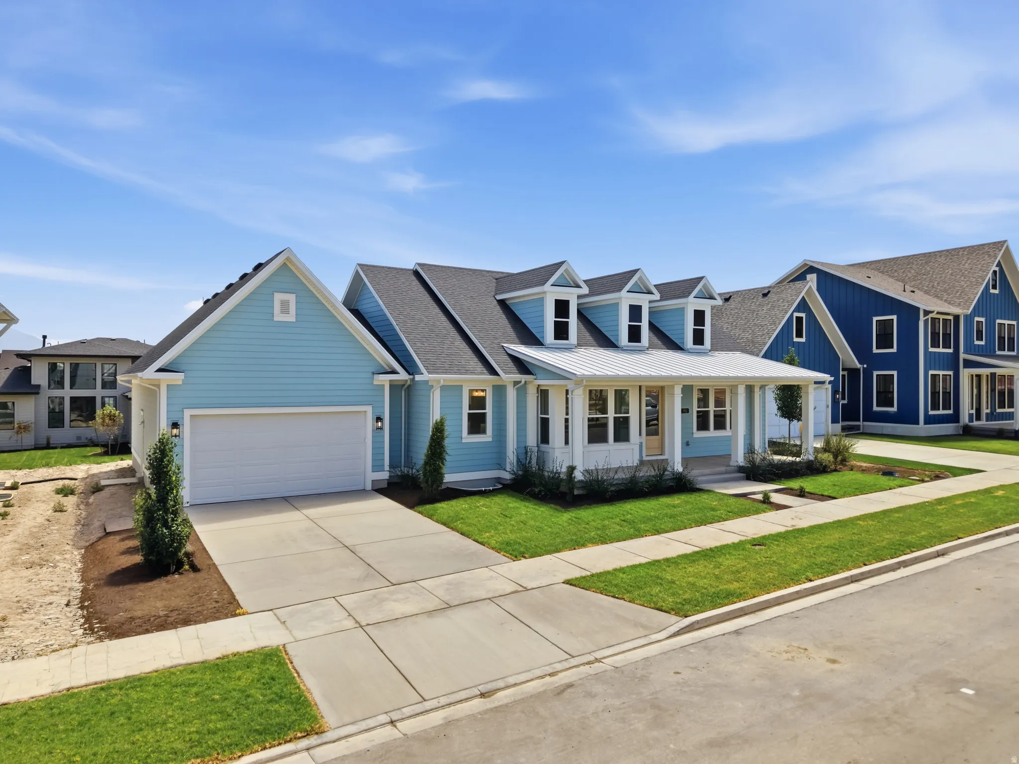 Light blue exterior siding with white trim, a covered front porch featuring white columns, multiple dormer windows, an attached two-car garage, and a concrete driveway