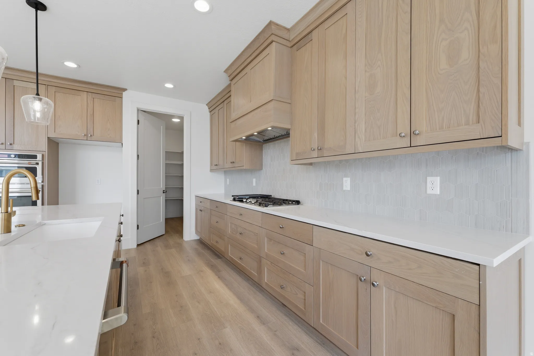 Light wood-finish cabinetry with crown molding, white countertops, built-in gas range, tile backsplash, and wood-finish flooring