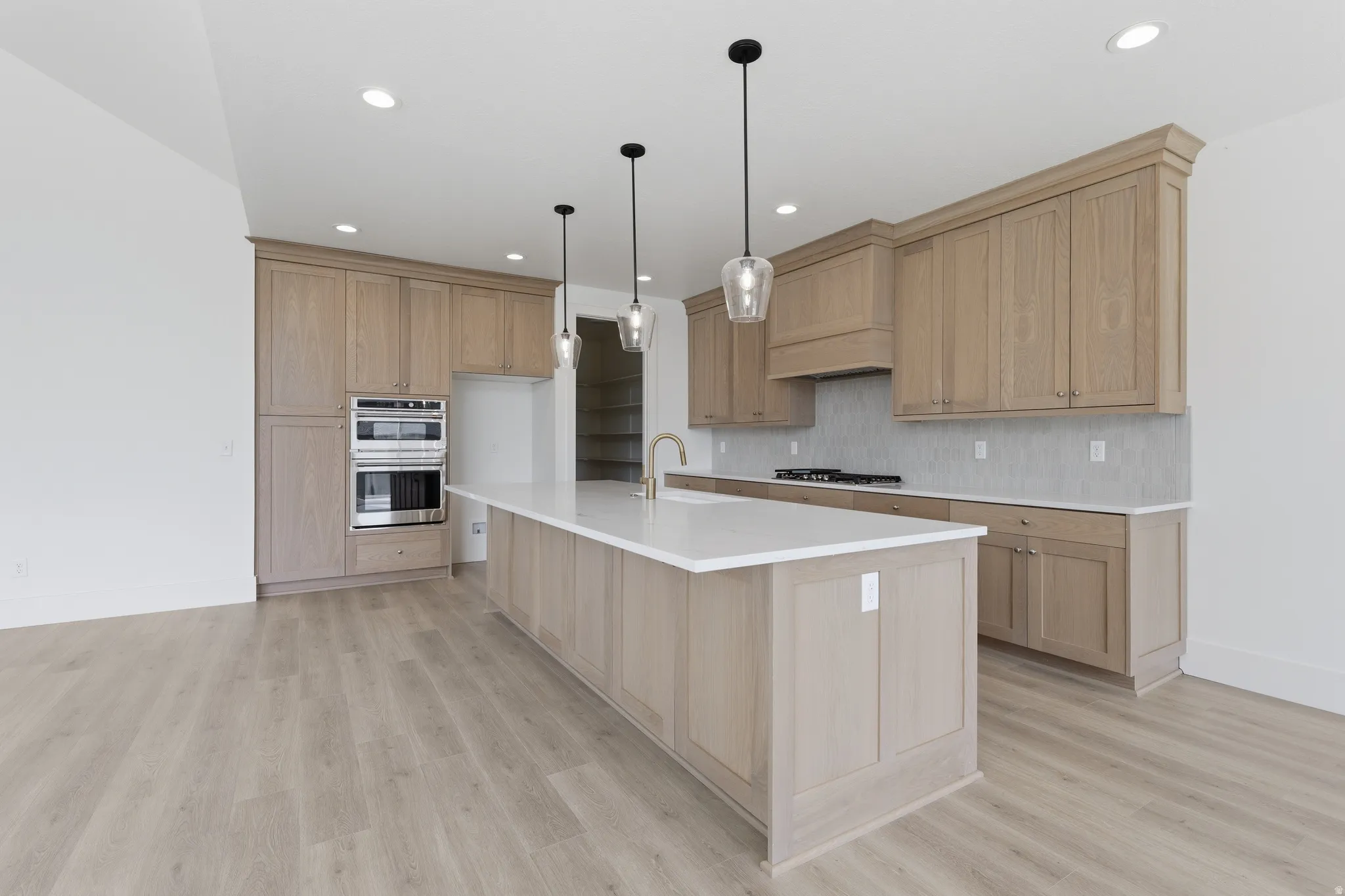 Kitchen featuring a large center island with a white countertop, wood-finish cabinetry, stainless steel double wall ovens, a gas cooktop, and recessed lighting