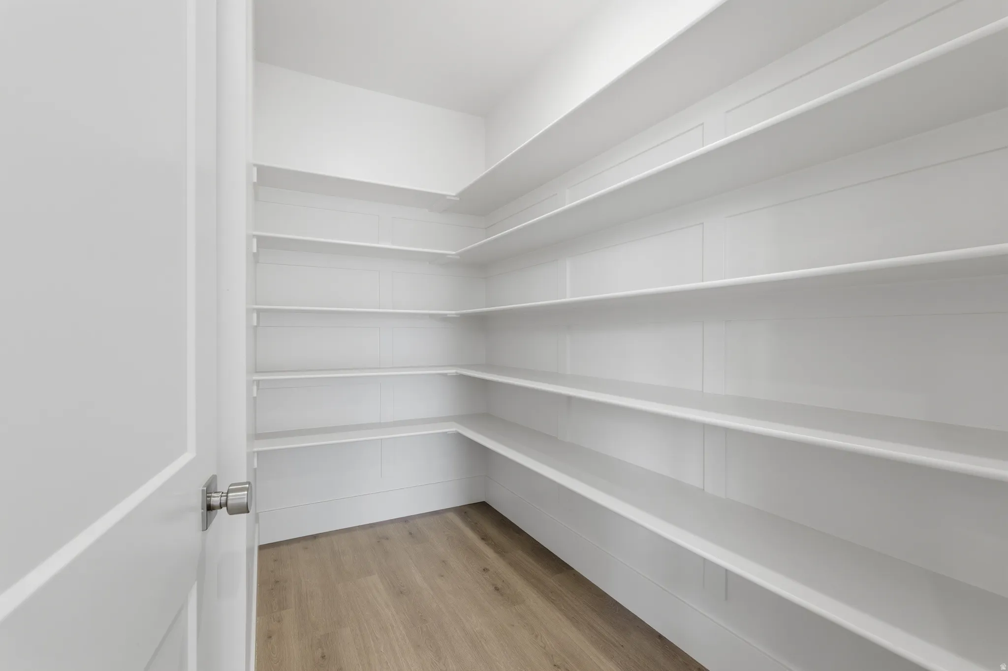 Expansive pantry featuring wrap-around shelving, clean white finishes, and wood-finish flooring