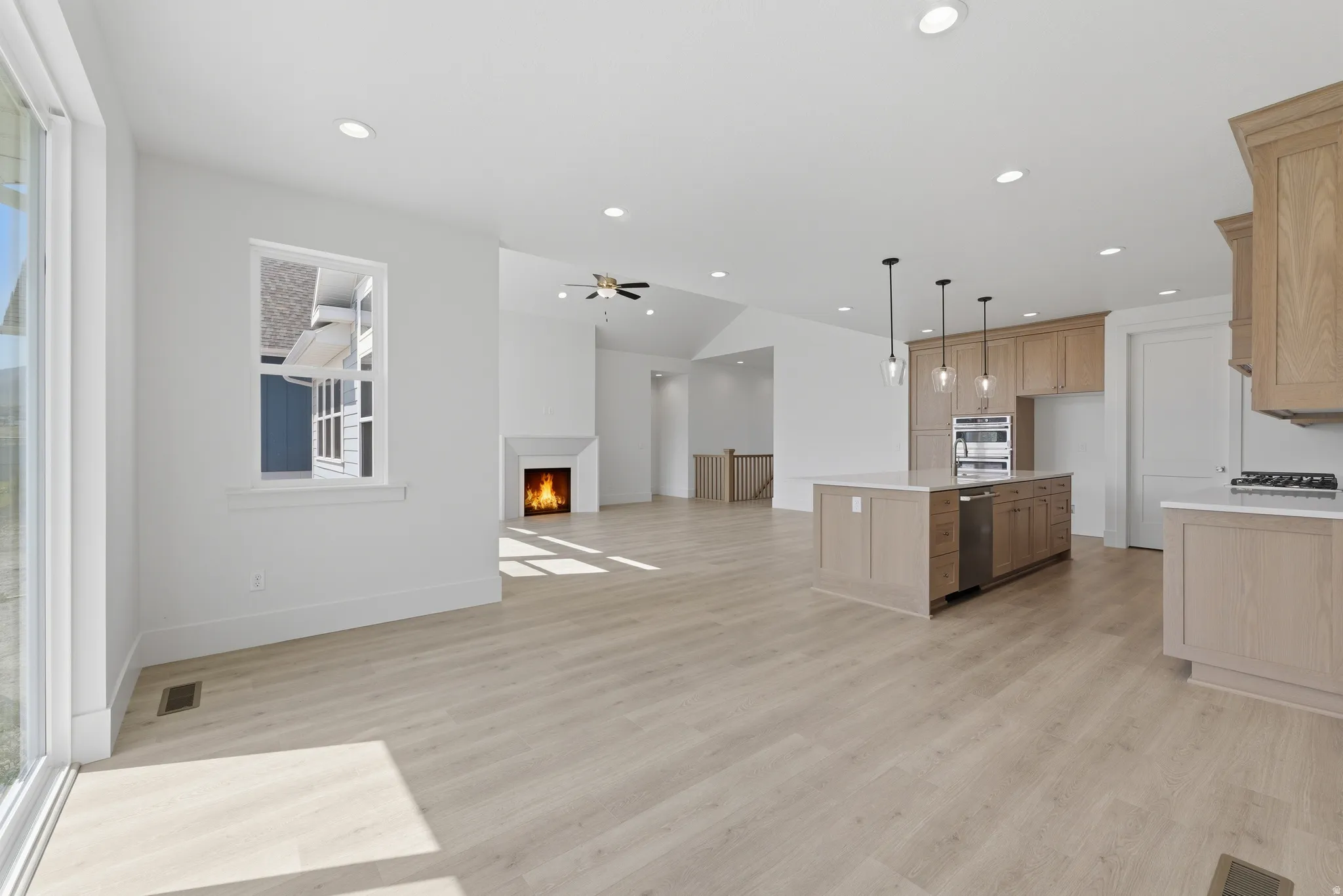 Open concept living space featuring wood-finish flooring, a contemporary fireplace, recessed lighting, and a kitchen island with pendant lighting