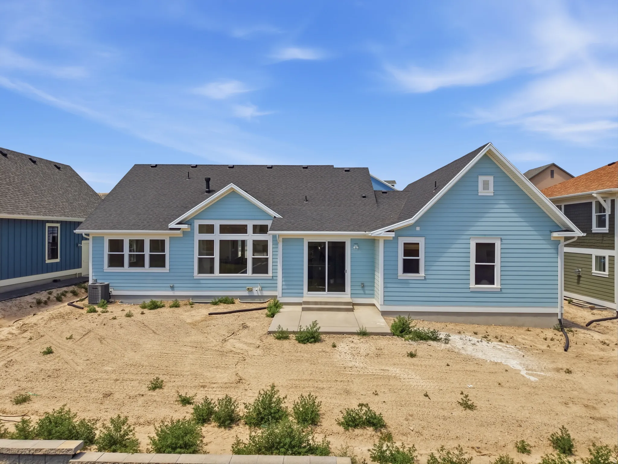 Rear exterior featuring light blue siding, multiple windows, a sliding glass door, an exterior patio, and a dark shingle roof