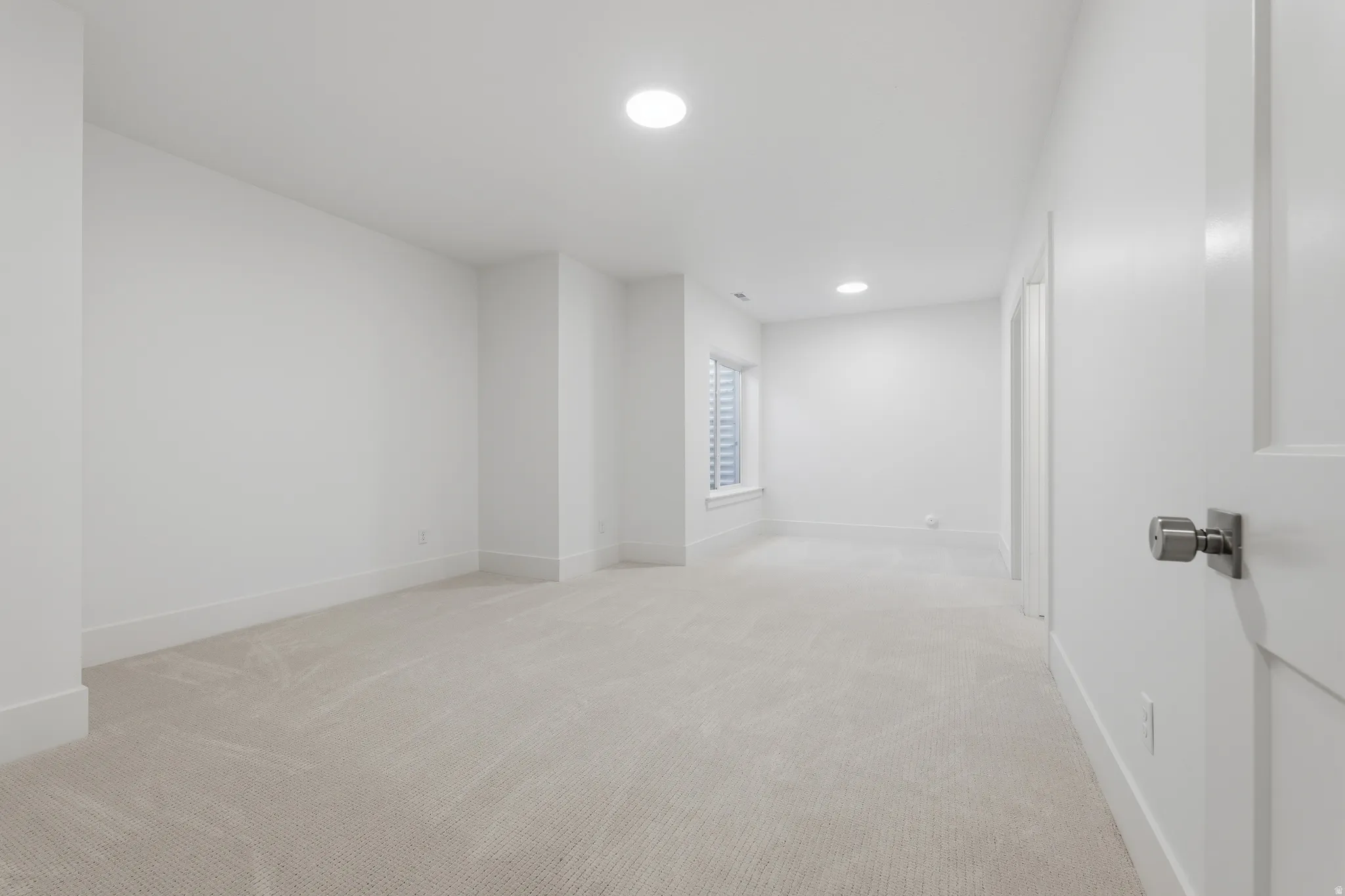 Basement bedroom with ensuite bathroom. Neutral tone carpet flooring with white walls, recessed ceiling lighting, and a single window