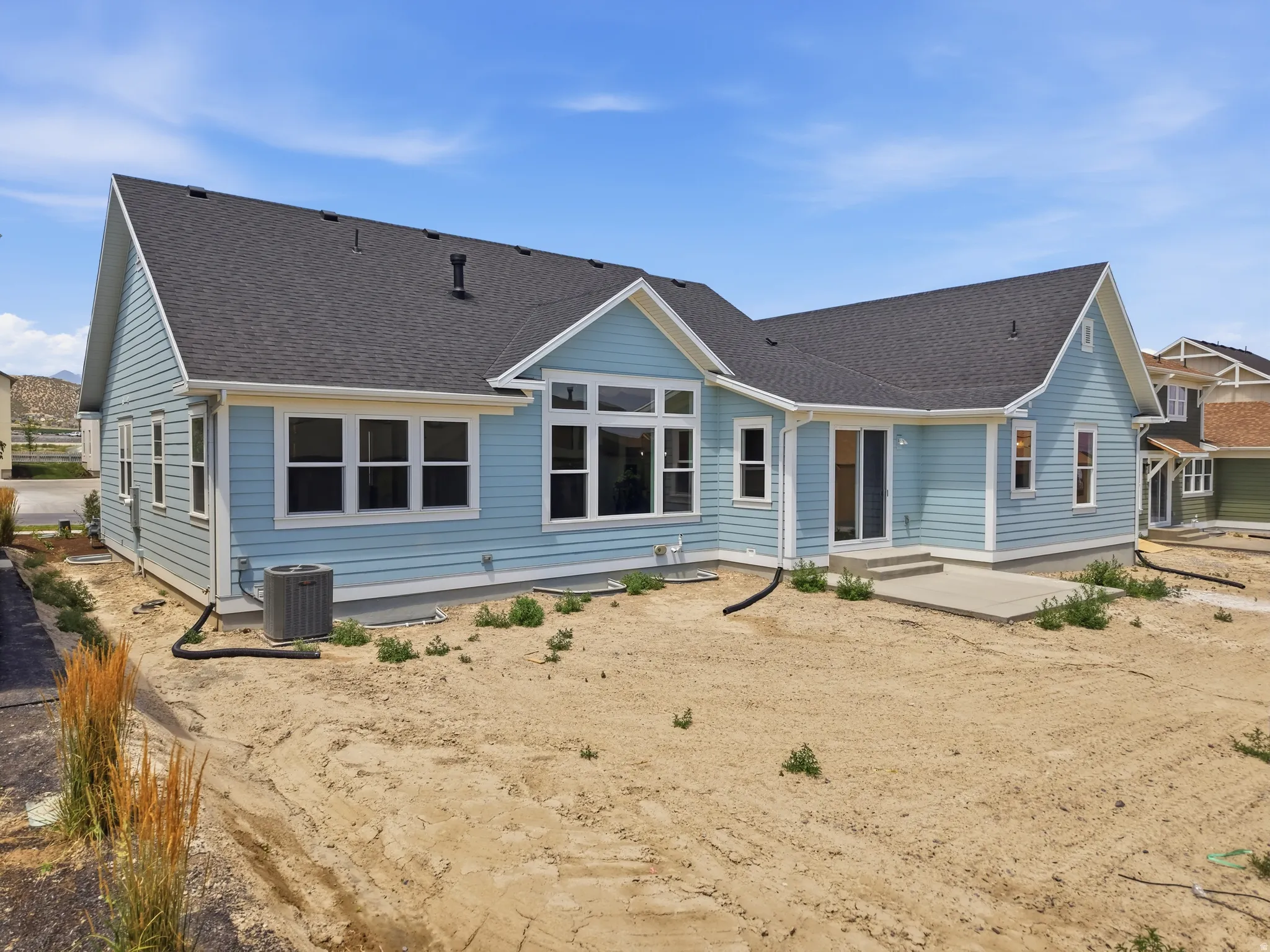 Light blue siding exterior with dark shingle roofing, multiple windows, and a concrete patio