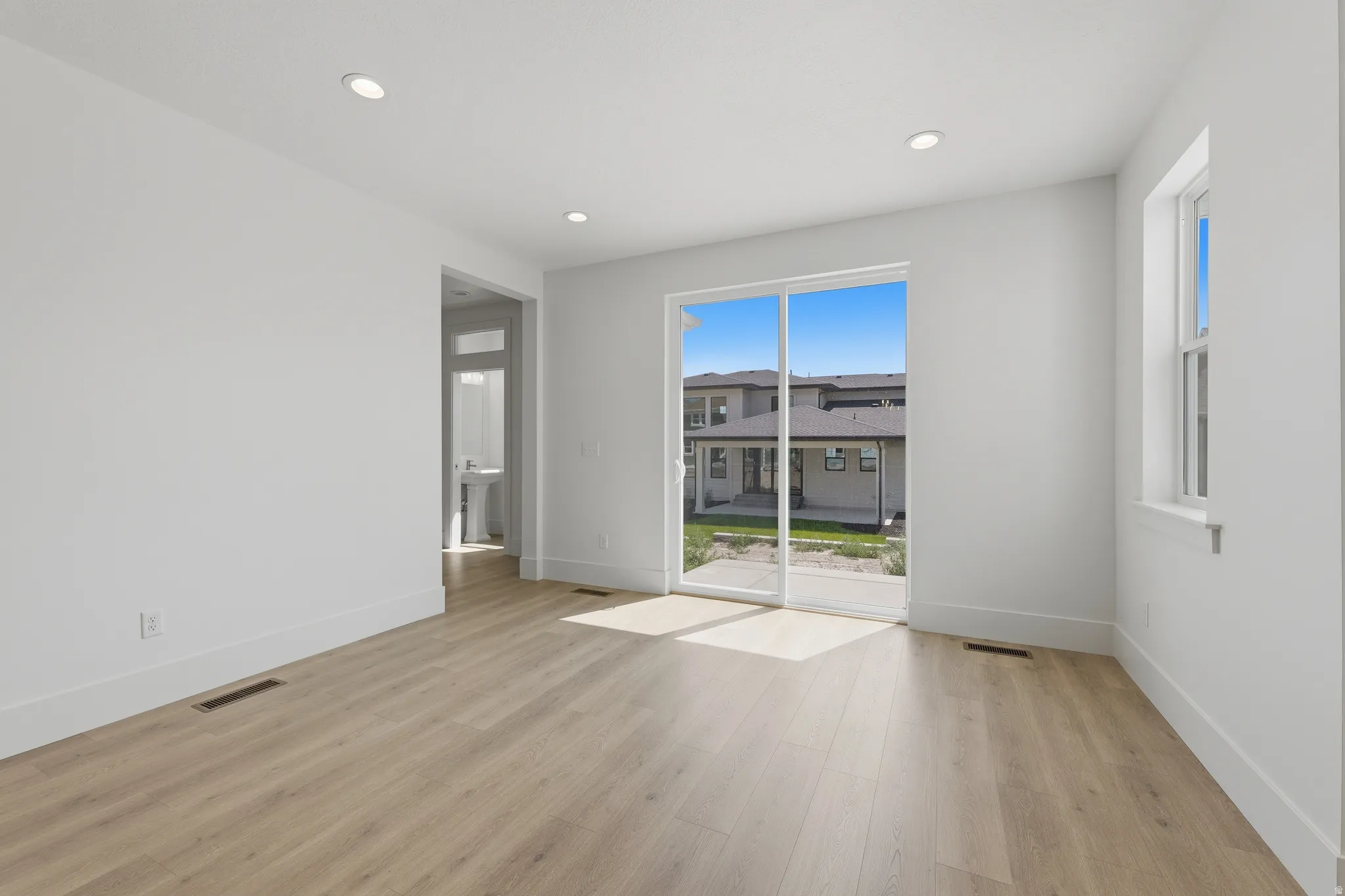 Recessed lighting, wood-finish flooring, white walls, large sliding glass door, and a single window