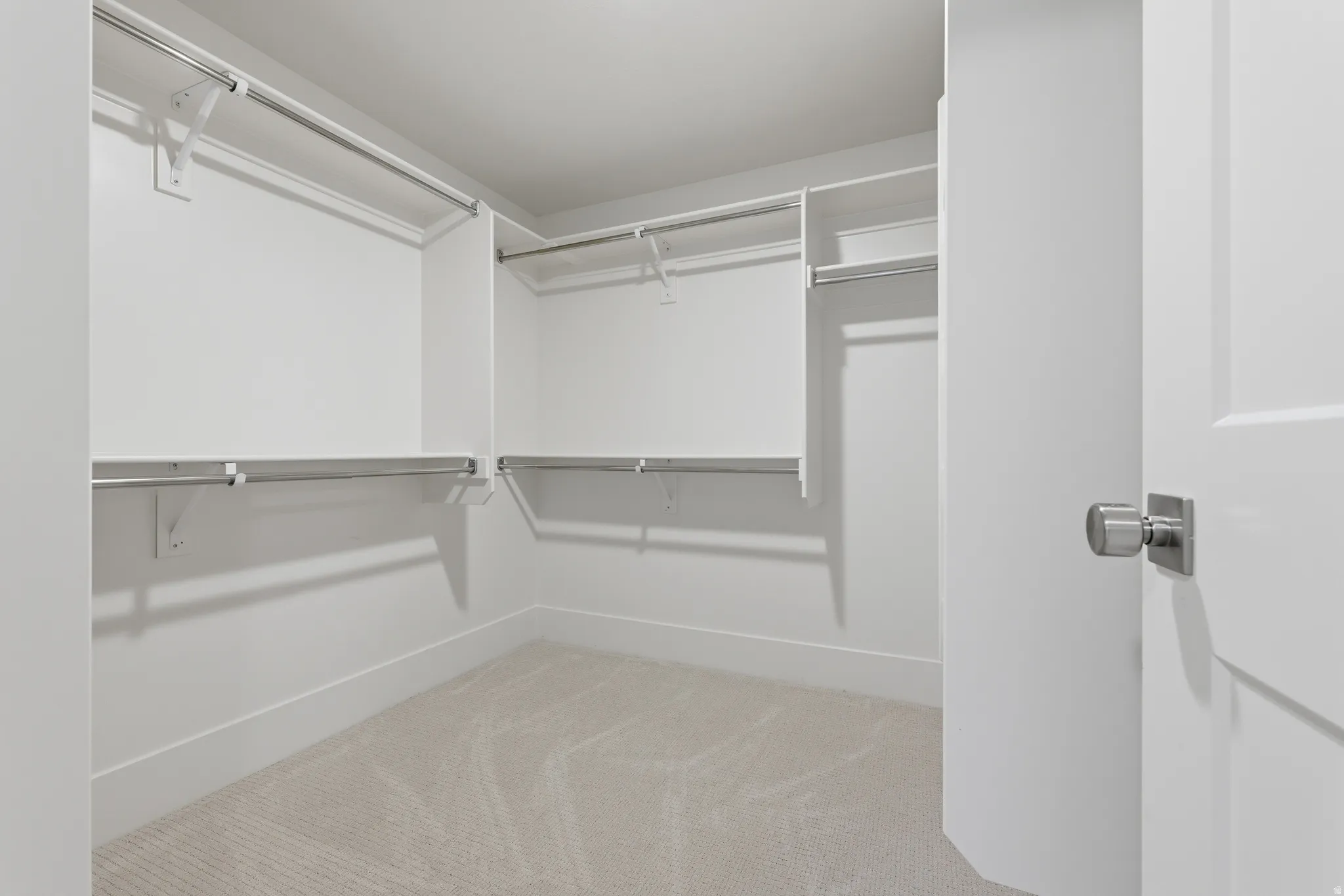 Walk-in closet with built-in shelving, multiple hanging rods, and light-toned carpeting