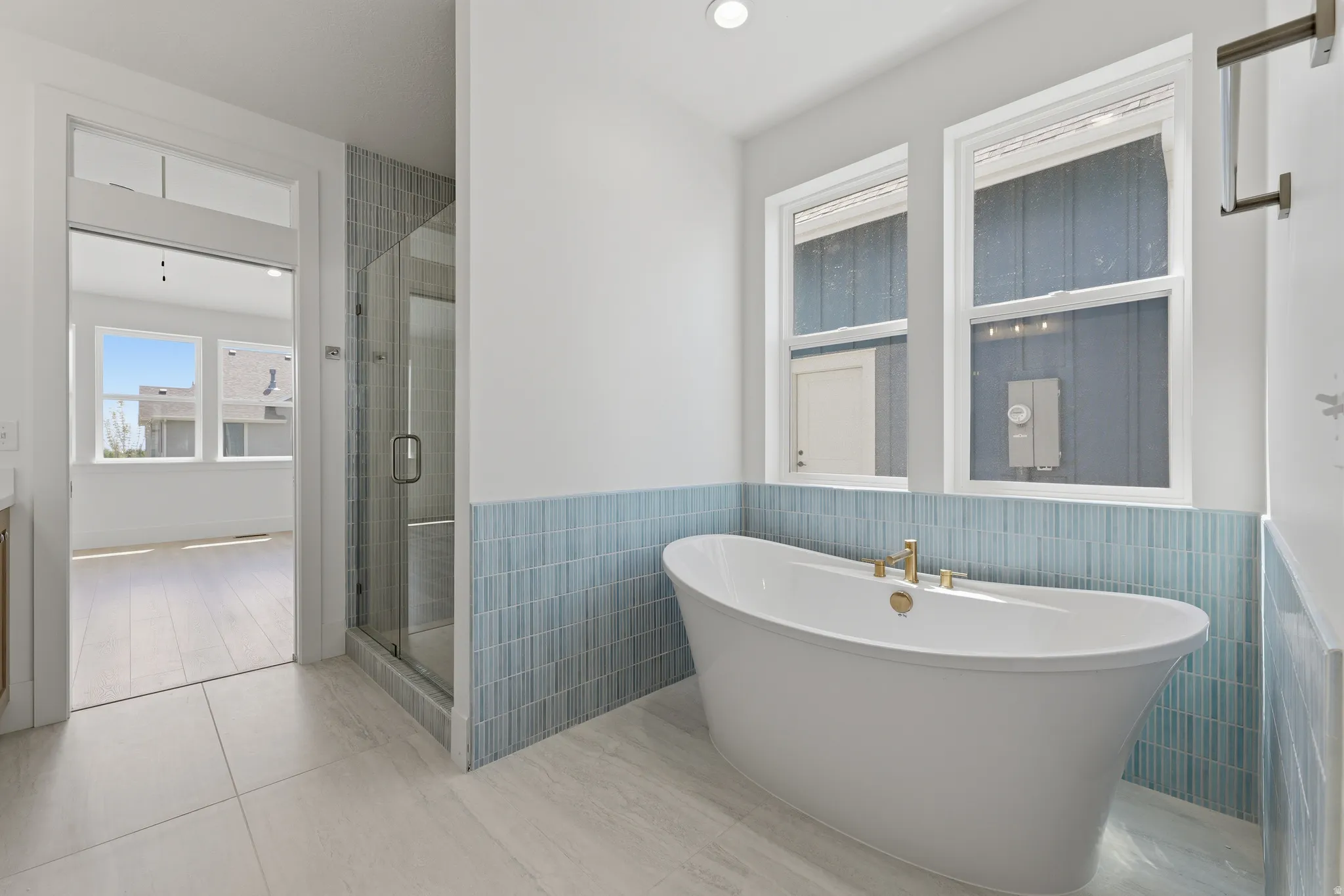 Primary Suite. Freestanding soaking tub with gold-finish fixtures, complemented by a glass-enclosed shower and tiled accent wall