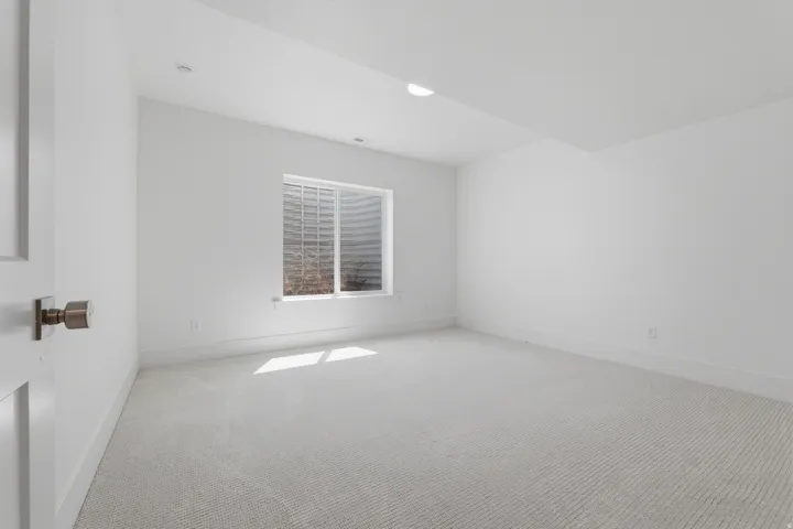 Recessed lighting, white walls, light-colored carpet, egress window, and a white door with a round knob
