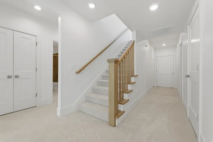 Carpeted flooring extending through a hallway and staircase with wood-finish handrails and newel posts