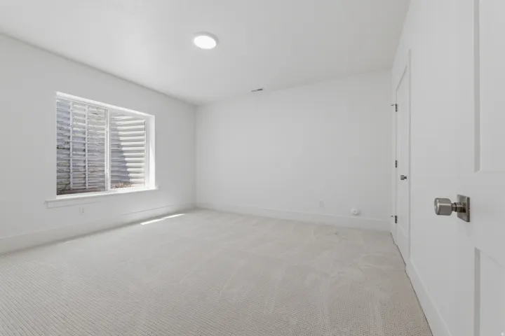 White walls, light-colored carpeting, recessed lighting, and a window with a window well