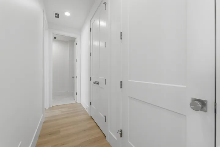 Hallway with wood-finish flooring, white walls, recessed lighting, and panel doors with brushed nickel hardware