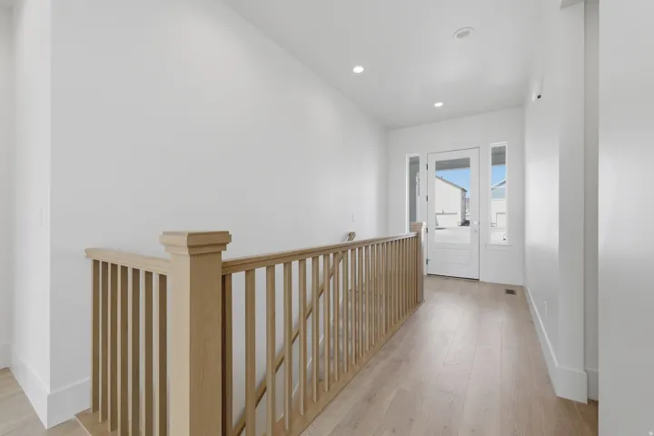 Light wood-finish flooring, recessed lighting, natural wood-tone staircase railing, white painted trim, and a white front entry door with side lites