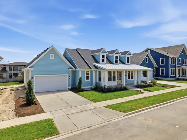 Light blue exterior siding with white trim, a covered front porch featuring white columns, multiple dormer windows, an attached two-car garage, and a concrete driveway