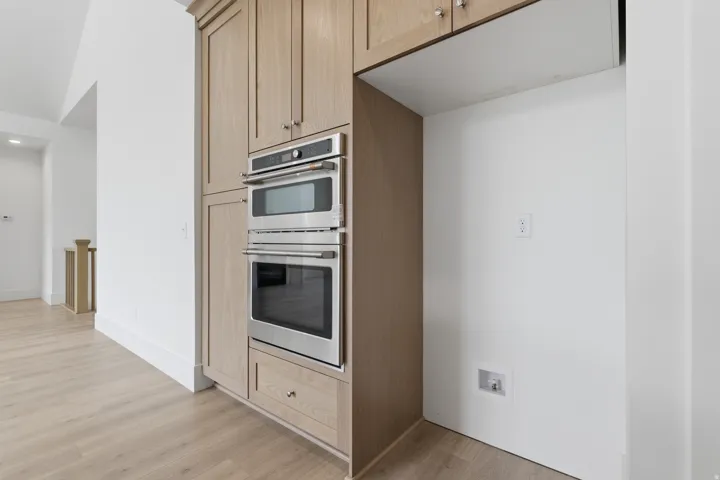 Built-in stainless steel double ovens, custom wood cabinetry with brushed nickel hardware, and wood-finish flooring