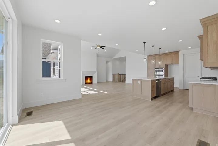 Open concept living space featuring wood-finish flooring, a contemporary fireplace, recessed lighting, and a kitchen island with pendant lighting