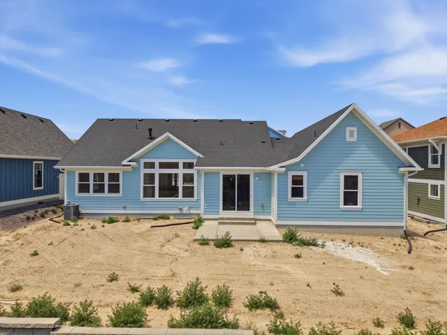 Rear exterior featuring light blue siding, multiple windows, a sliding glass door, an exterior patio, and a dark shingle roof