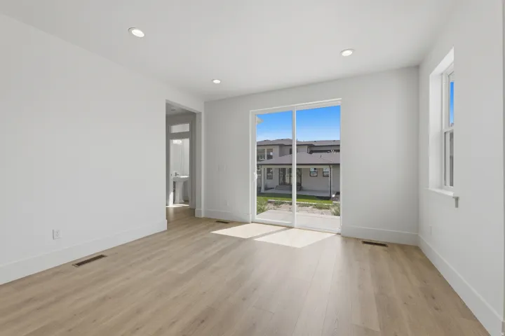 Recessed lighting, wood-finish flooring, white walls, large sliding glass door, and a single window