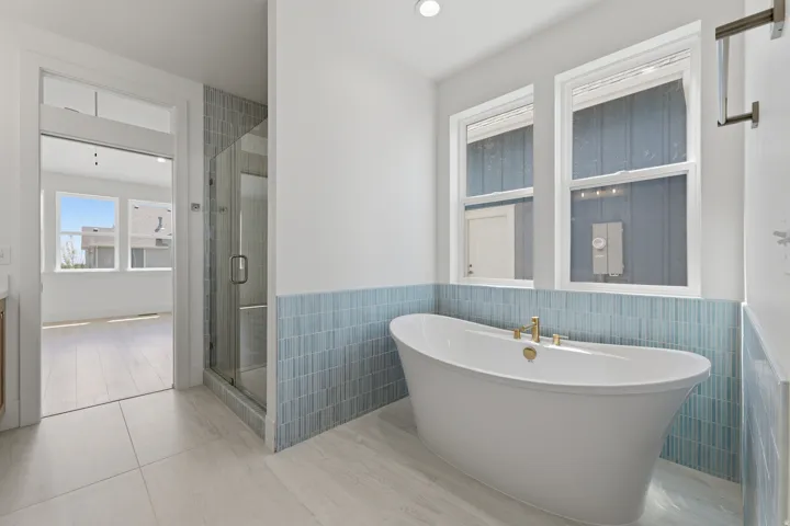 Primary Suite. Freestanding soaking tub with gold-finish fixtures, complemented by a glass-enclosed shower and tiled accent wall