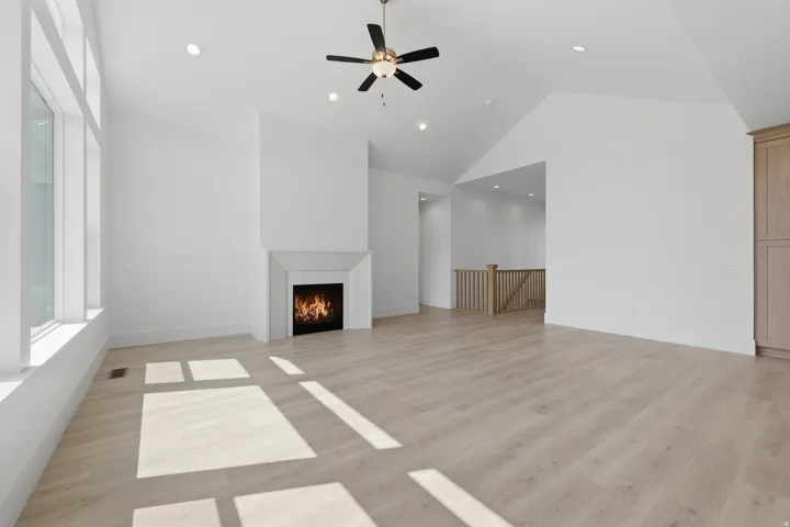 Vaulted ceiling with recessed lighting and ceiling fan, large windows, fireplace with mantel, wood-finish flooring, and built-in cabinetry