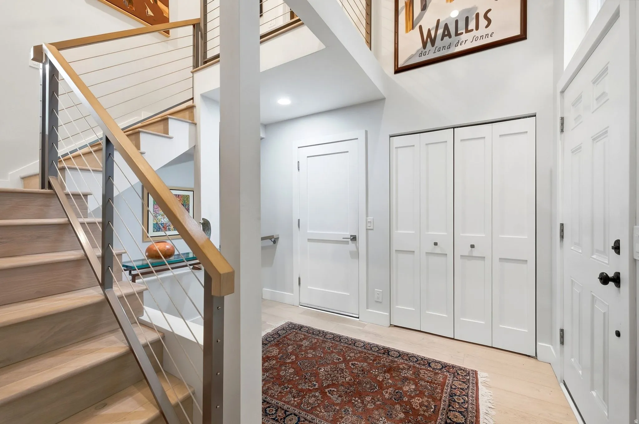 Hardwood staircase with cable railing, light wood-finish flooring, and white paneled doors