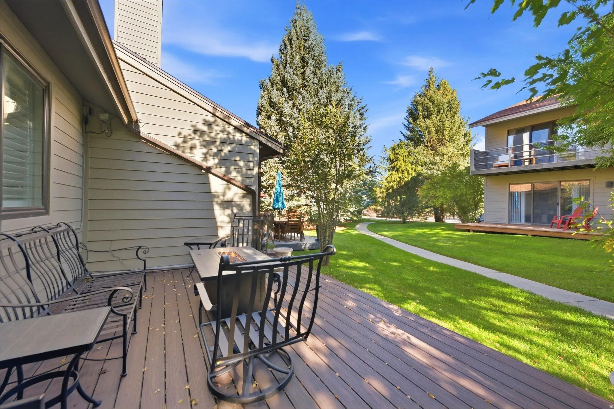 Expansive composite deck with exterior siding, manicured lawn, and mature trees