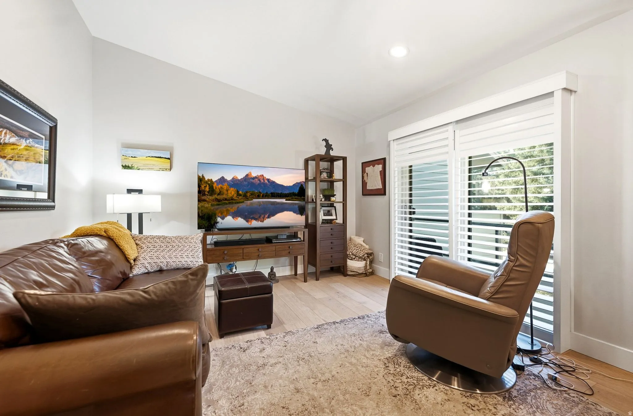 Vaulted ceiling, light wood-finish flooring, white walls, recessed ceiling lighting, and sliding glass doors with white plantation shutters