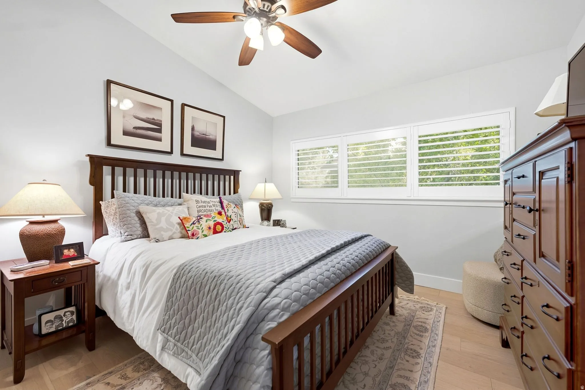 Vaulted ceiling, ceiling fan with integrated lighting, multiple windows with plantation shutters, light wood-finish flooring
