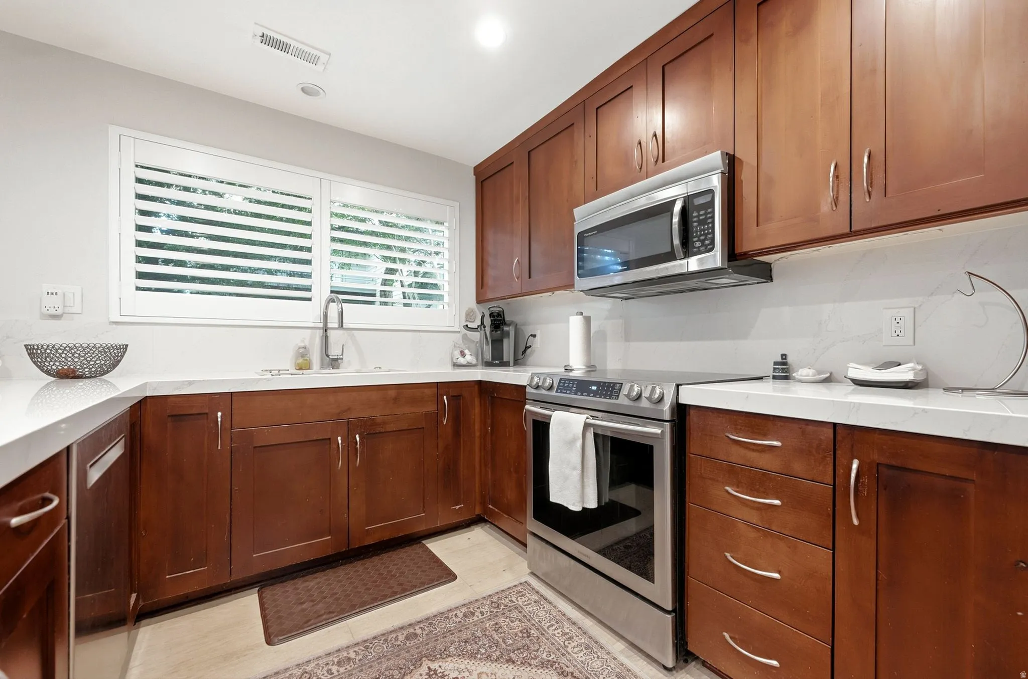 Wood-finish cabinetry with stainless steel hardware, white countertops, stainless steel appliances, and a white tile backsplash