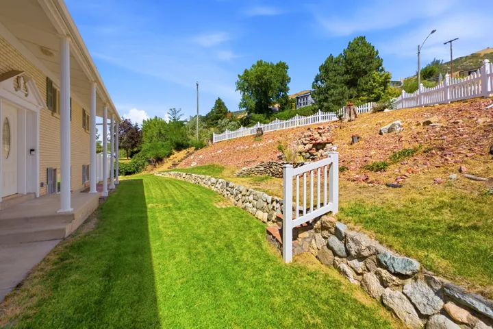 Expansive side yard featuring a manicured lawn, stone retaining wall, and a white picket fence