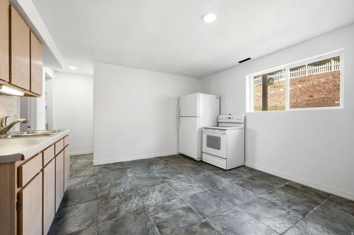 Kitchen featuring a stainless steel double basin sink, light wood-finish cabinetry, and white appliances