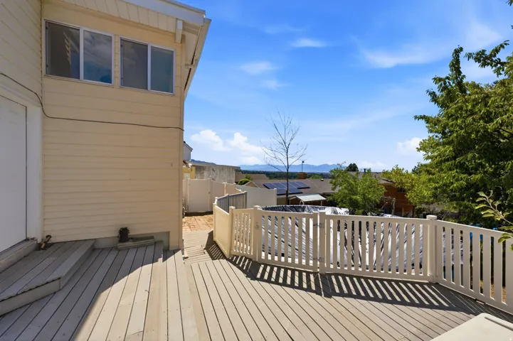 Expansive wood-finish deck with white railing, light-colored siding, and visible upper-level windows