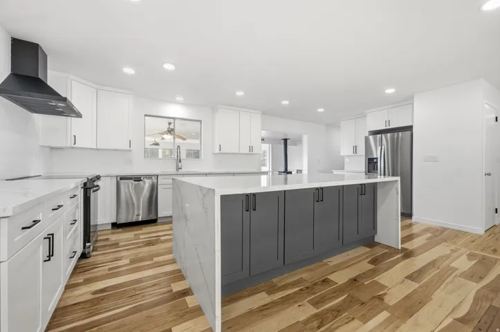 Wood-finish flooring throughout, white upper cabinetry, and a central island with gray lower cabinetry