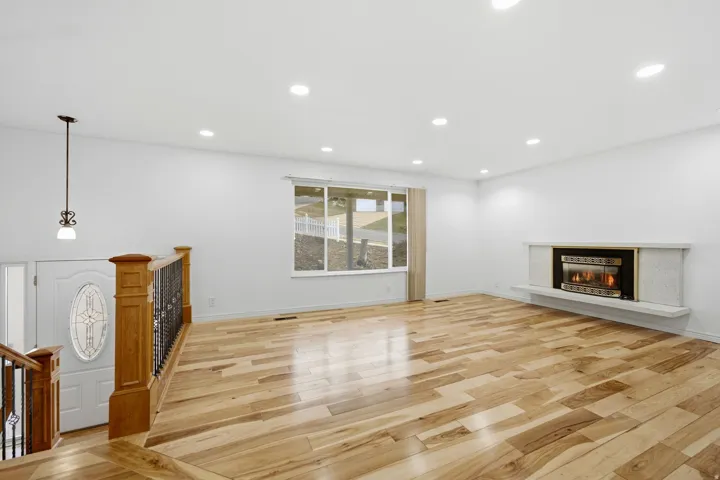 Hardwood flooring, recessed lighting, white walls, and a built-in fireplace with a stone hearth
