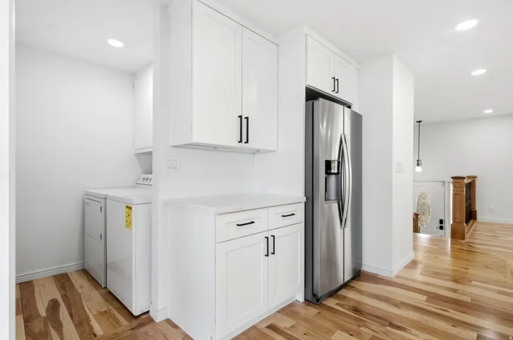 White cabinetry with matte black hardware, integrated stainless steel refrigerator, light-toned wood-finish flooring, and recessed lighting