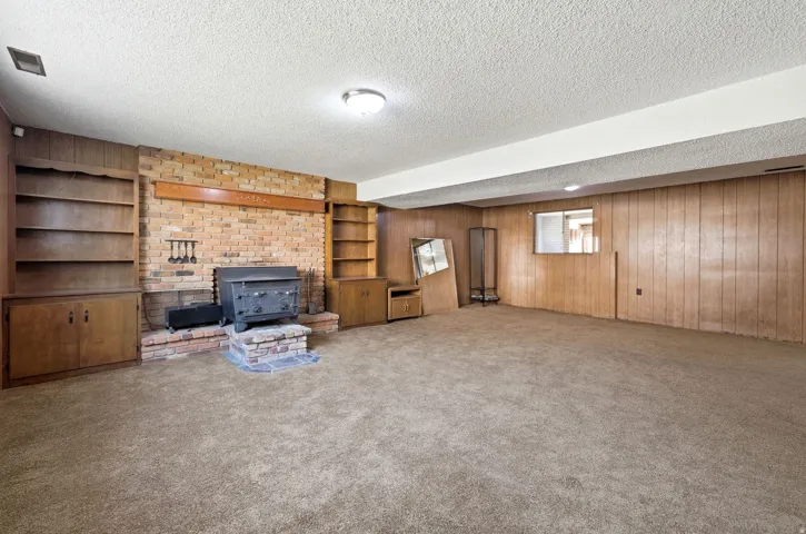 Brick fireplace with stone base, wood-paneled walls, built-in shelving, and carpeted flooring