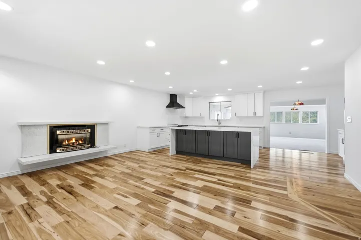 Open-concept living area with wood-finish flooring, recessed lighting, a built-in fireplace, and a kitchen island with stone countertops