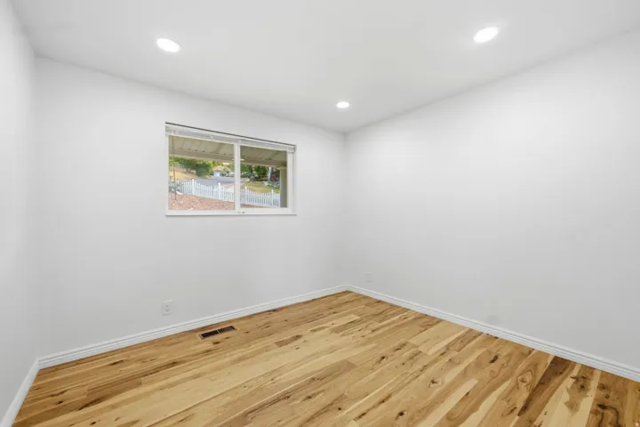 Recessed lighting, wood-finish flooring, white walls, and a window with a white frame