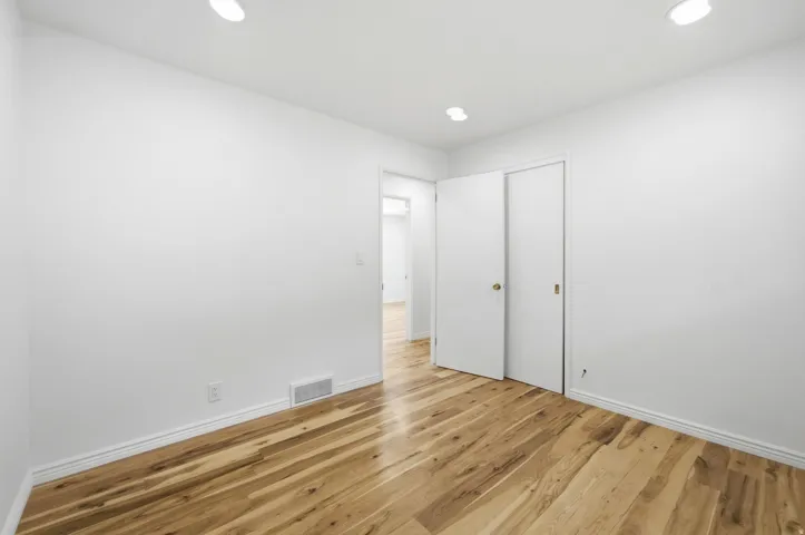 Recessed ceiling lighting, wood-finish flooring, white walls, and a white sliding closet door