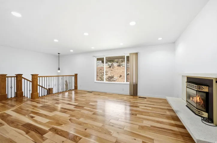 Expansive living area featuring wood-finish flooring, recessed lighting, and a corner fireplace with a light-toned hearth