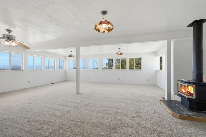 Expansive room featuring multiple windows, neutral carpeting, a wood-burning stove with a hearth, recessed lighting, and a ceiling fan