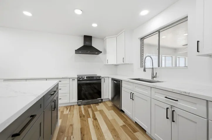 Kitchen featuring white cabinetry, a kitchen island with dark cabinetry, wood-finish flooring, stainless steel appliances, and white countertops