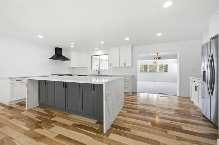 Kitchen featuring a large island with two-tone cabinetry and waterfall edge, stainless steel appliances, recessed lighting, and wood-finish flooring