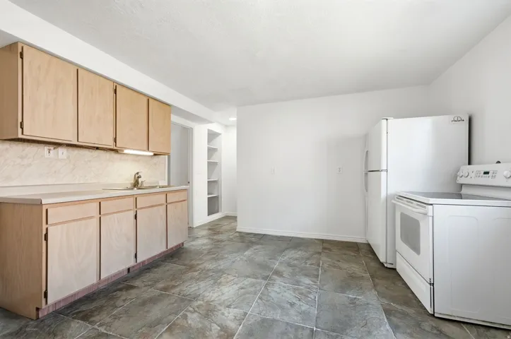 Kitchen featuring light wood cabinetry, a light-toned countertop, a stainless steel sink, and white appliances