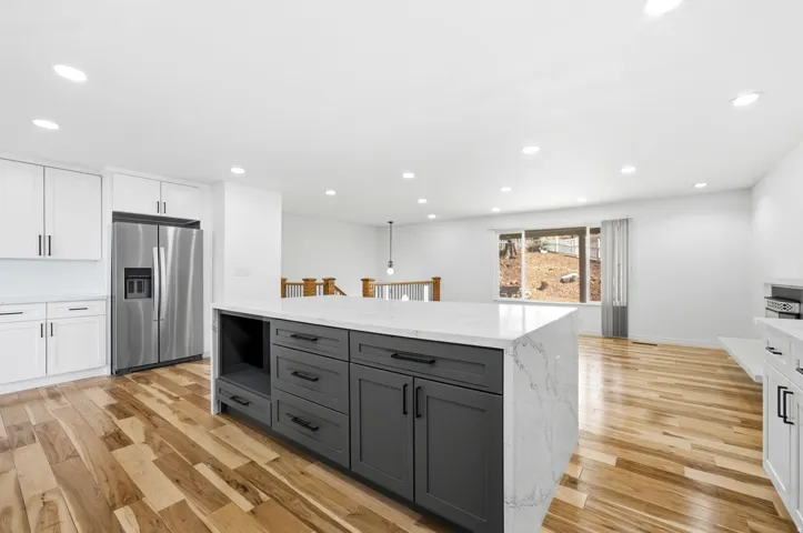 Kitchen featuring a large island with a light-toned countertop, white cabinetry with dark hardware, stainless steel refrigerator, and wood-finish flooring