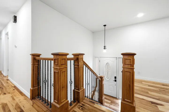 Hardwood flooring, wood staircase with wrought iron balusters, white paneled door with oval glass insert, pendant light fixture, recessed ceiling lighting