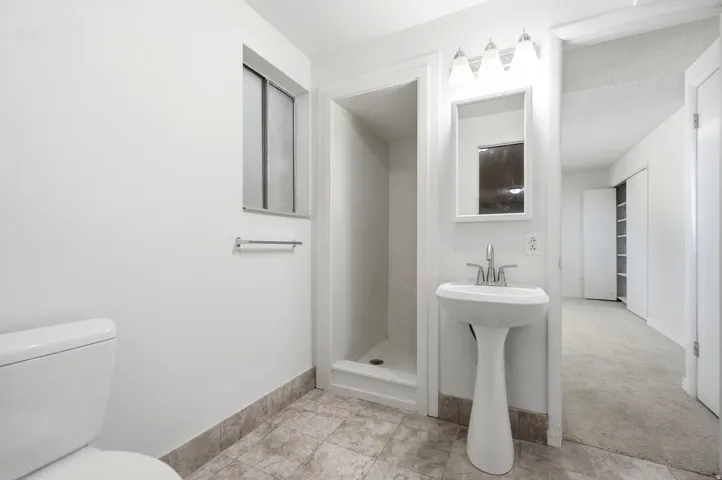 Pedestal sink with chrome faucet, wall-mounted mirror, three-light vanity fixture, and tiled flooring