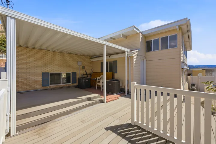 Expansive outdoor deck with white railing, covered patio area, and brick exterior accent