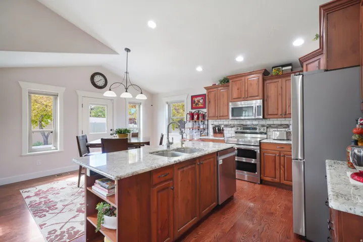 Vaulted ceiling kitchen featuring wood-finish flooring, granite countertops, wood cabinetry, and stainless steel appliances
