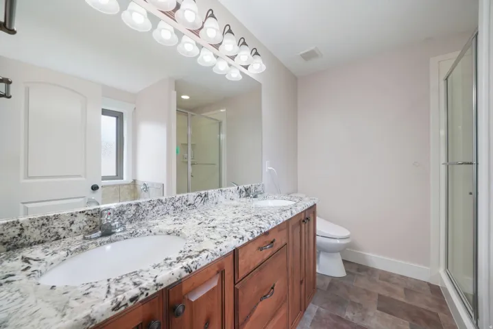 Dual vanity with wood cabinetry, speckled stone countertop, and undermount sinks